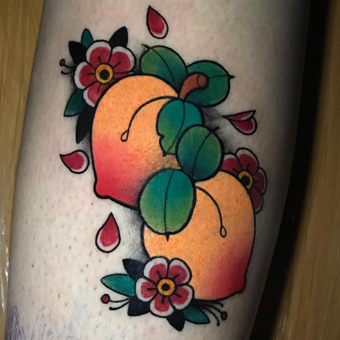 Vibrant traditional-style tattoo of two peaches surrounded by leaves and red flowers